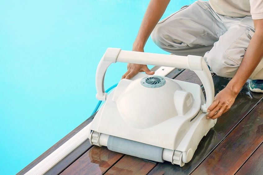 Technicien installant un robot nettoyeur de piscine blanc, représentant un Best Hygiène matériel pour l'entretien des bassins