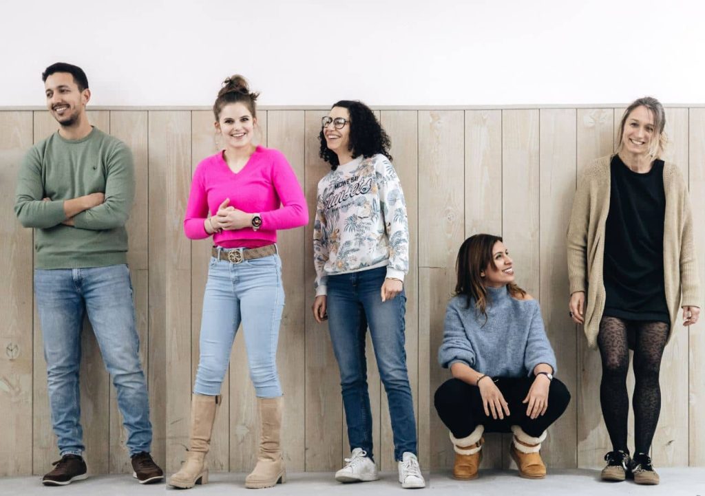 Groupe de cinq personnes souriantes, potentiellement des participants à une formation de théâtre, posant devant un mur en bois clair.