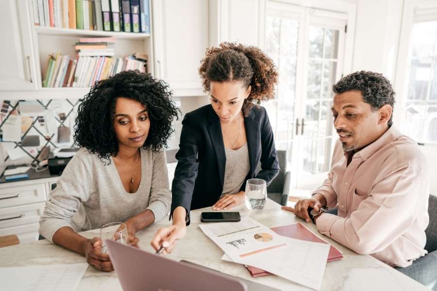 Trois personnes consultent un ordinateur portable et des documents autour d'une table, illustrant l'usage des applications mobiles dans un contexte professionnel.