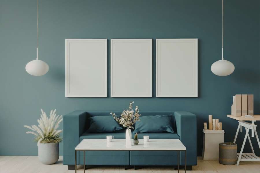 Salon moderne bleu canard avec canapé assorti, deux suspensions rondes blanches et cadres muraux pour éclairer son salon avec élégance.