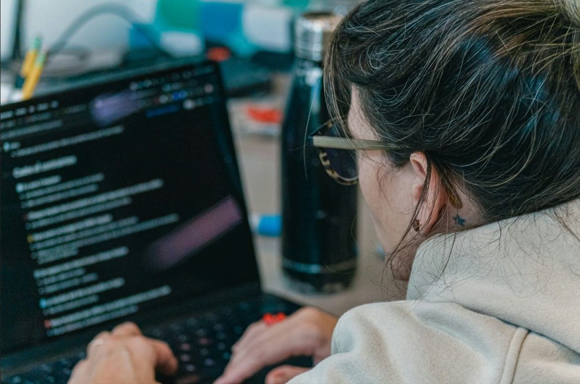 Une femme de dos travaillant sur son ordinateur portable avec un document affiché à l'écran, illustrant l'utilisation d'un guide débutant IA pour apprendre les bases de l'intelligence artificielle.
