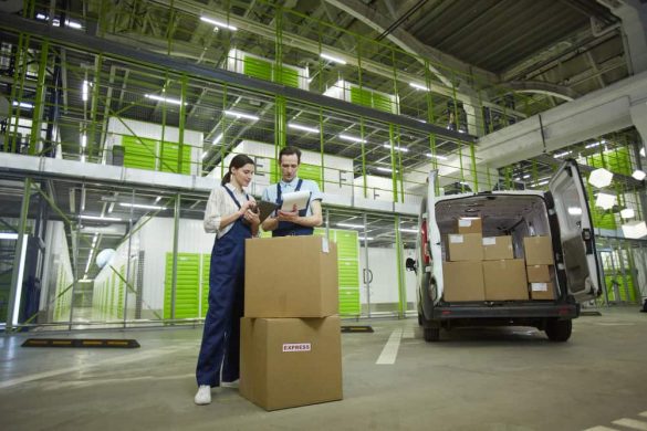 Deux professionnels en salopette vérifiant une liste d'inventaire devant une camionnette de livraison chargée de cartons, dans le cadre d'un déménagement industriel