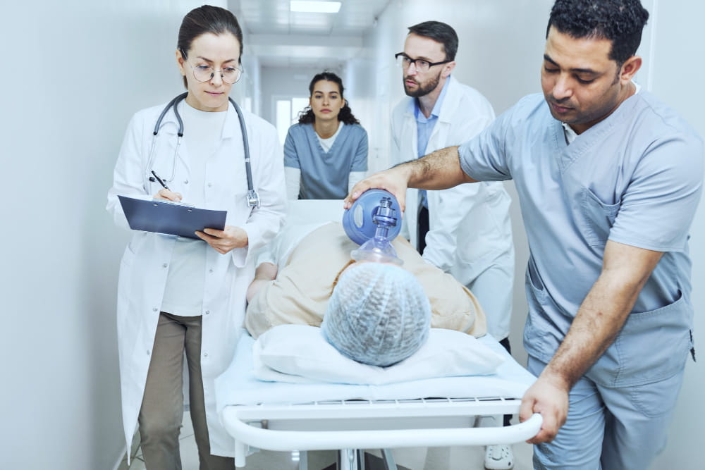 Équipe médicale transportant un patient sur un brancard dans un couloir d'hôpital avec un médecin en urgence prodiguant des soins respiratoires.