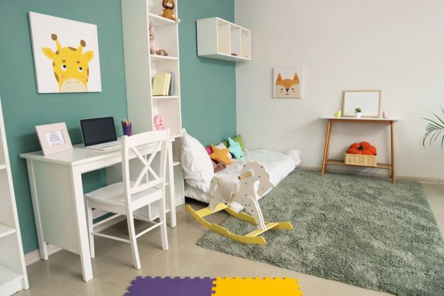 Une chambre d'enfant lumineuse avec un bureau, un tapis vert et un cheval à bascule dans une ambiance douce.