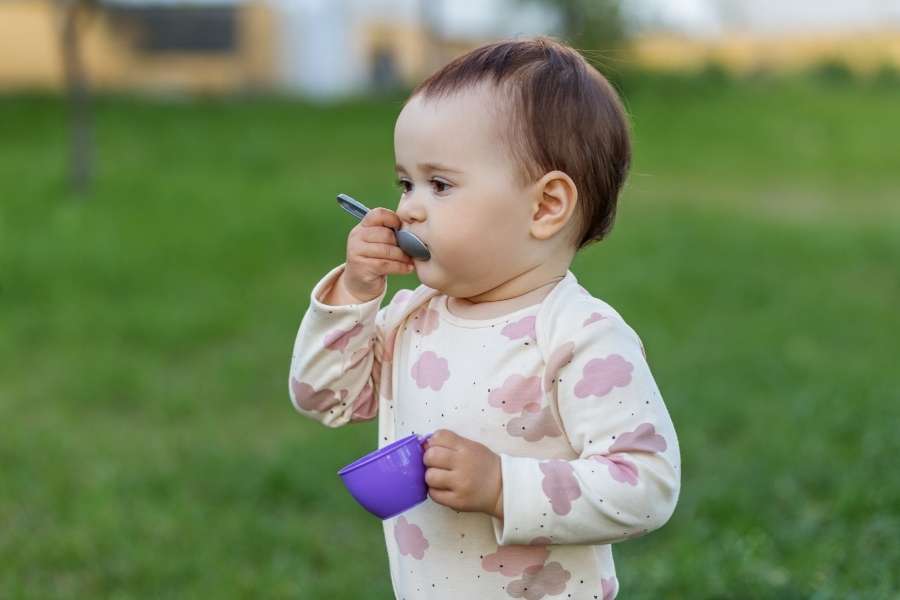 Un jeune enfant apprend à manger tout seul avec une cuillère, illustrant l'autonomie des enfants au quotidien.