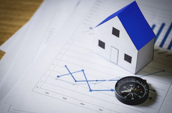 Petite maison en papier et boussole posées sur des graphiques financiers illustrant le Baromètre des Prix Immobiliers Notaires.