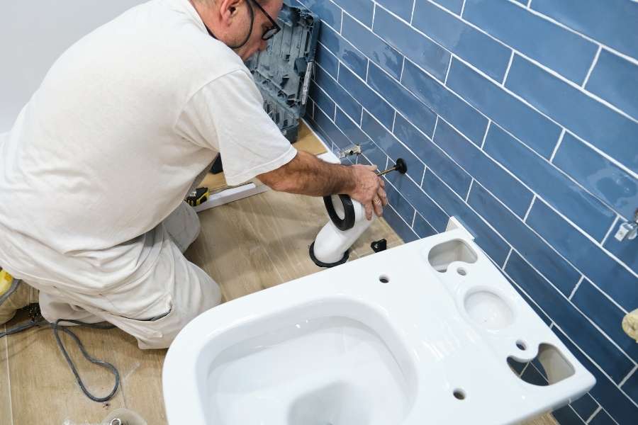 Un plombier installe le système d'évacuation d'un WC suspendu dans une salle de bain en rénovation.