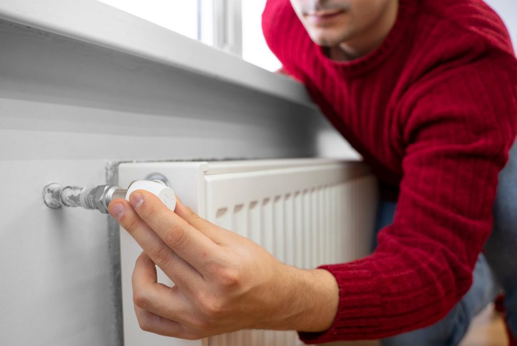 Un homme ajuste le thermostat d'un radiateur blanc, illustrant des conseils d un pro pour économiser chauffage.